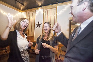 Council Member Laura Morrison and Travis County Republican Party Vice Chair Roger Borgelt exchange high-fives at the housing campaign's election watch party at Scholz Garten, while HousingWorks' Mandy De Mayo looks on.