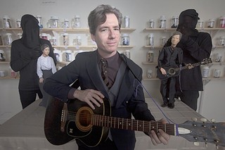 Adam Sultan the man with his puppet doppelganger and his wife before a wall of jars