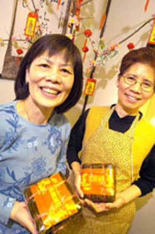 Tâm Deli owners Tâm Bui (l) and Tran Ngoc hold 
packages of <i>banh chung</i> in front of their good 
luck tree.