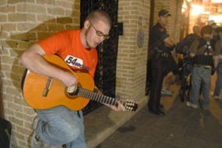Street musician Trevor Goodchild plays while a cop
watches. Goodchild says he was assaulted by cops
with a Taser while offering no resistance.