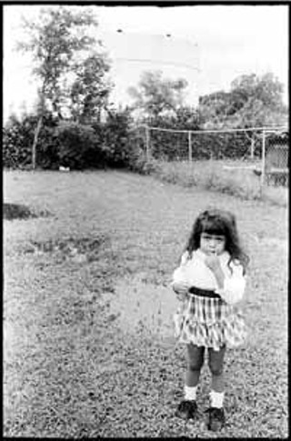 Jana Birchum: 1992. Aida Sotelo's back yard, which backs onto the East Austin gasoline tank farm. The farm leaked gasoline into the air and water supply, and people all over the area had headaches, nosebleeds, and various other forms of illness. An elementary school is two blocks away. Through community organizing, the gasoline companies involved, including Exxon, Citgo, Shell and others, were forced to close the tank farm and move it to a location away from populated areas.