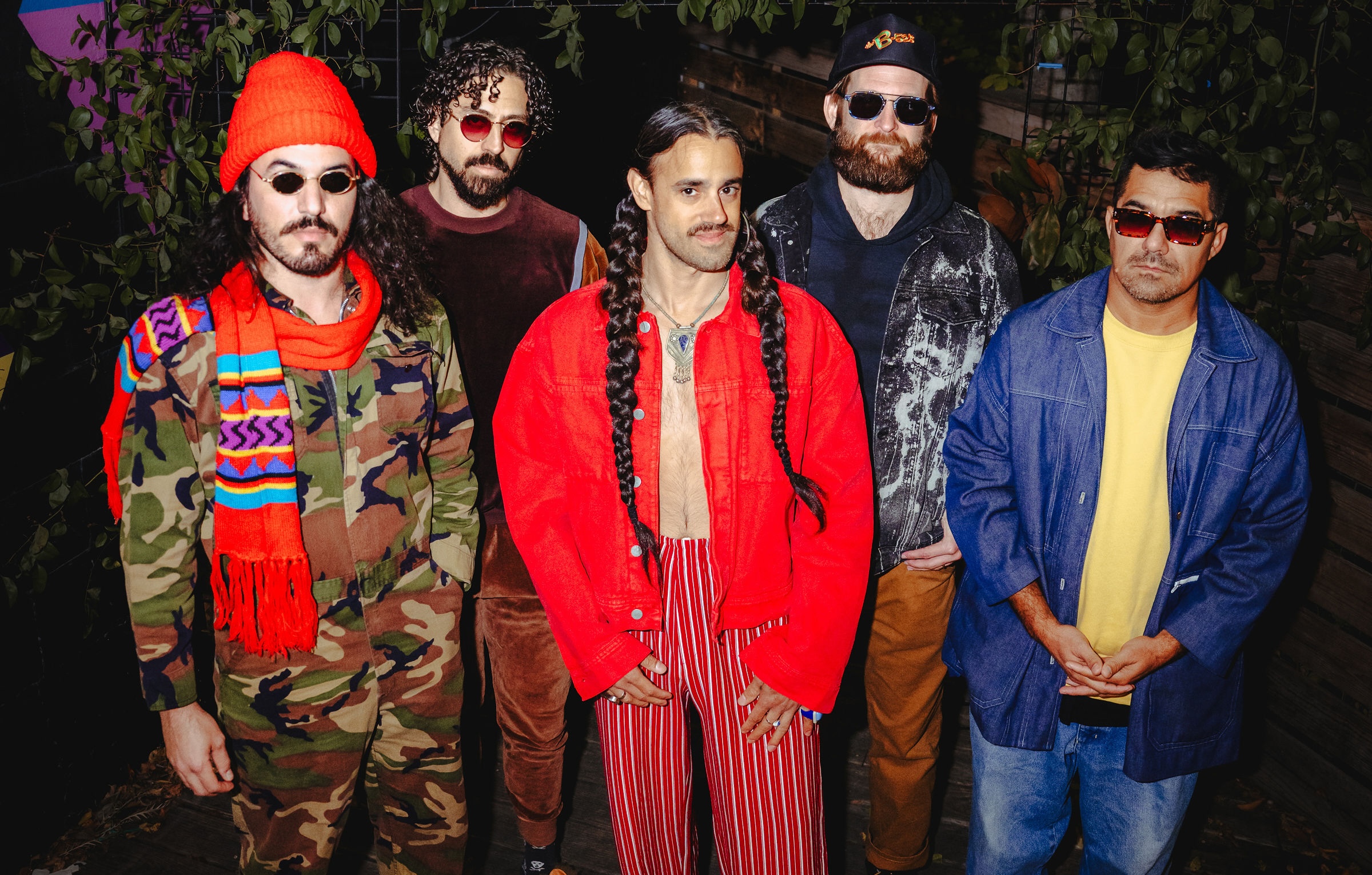 The five members of Austin band Starflake pose beneath leafy greenery in colorful jackets, sunglasses and red-and-white striped pants